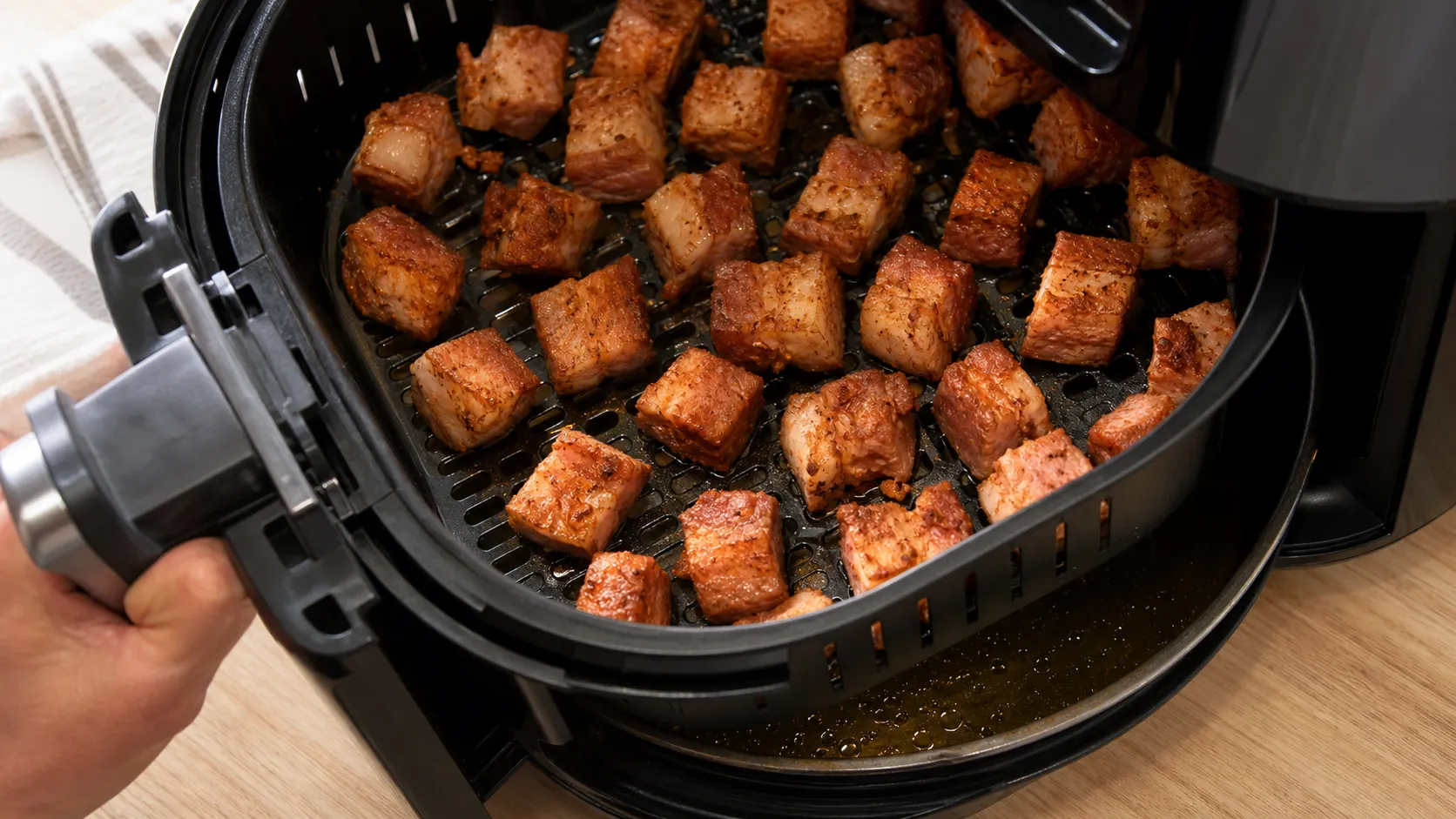 Pork belly cubes lying in a single layer in the basket, with rendered fat collecting below