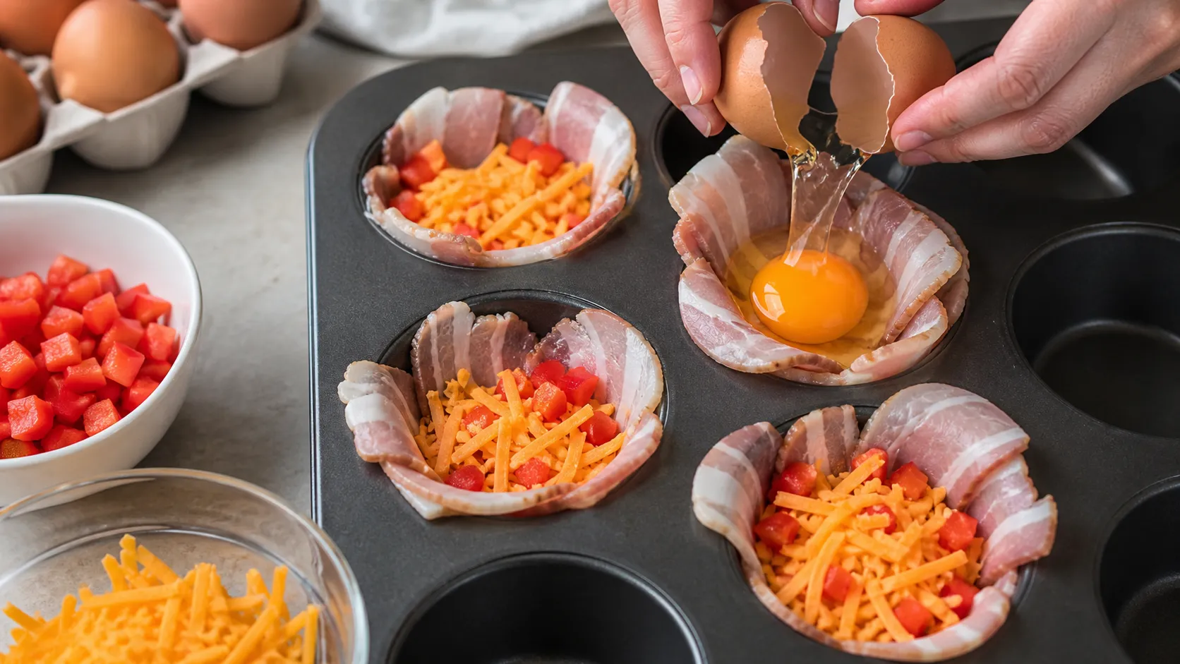 Bacon slices lining muffin tin wells, filled with bell pepper and cheddar before the egg goes in