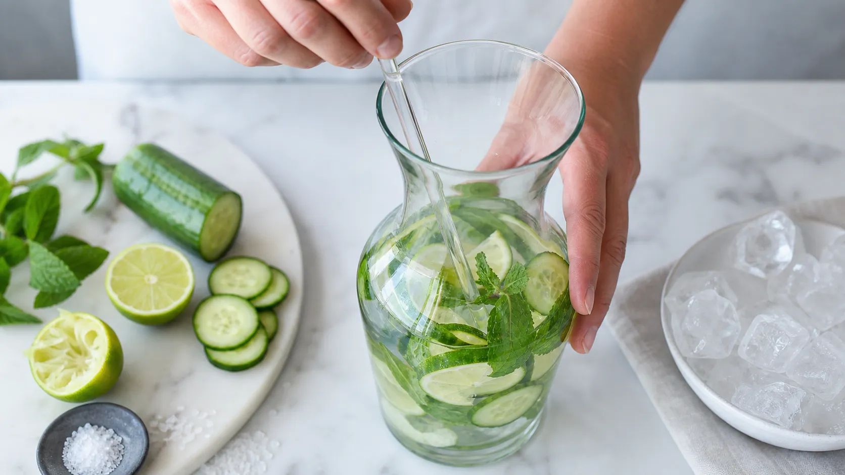Cucumber slices, lime juice and mint being stirred into a carafe of water