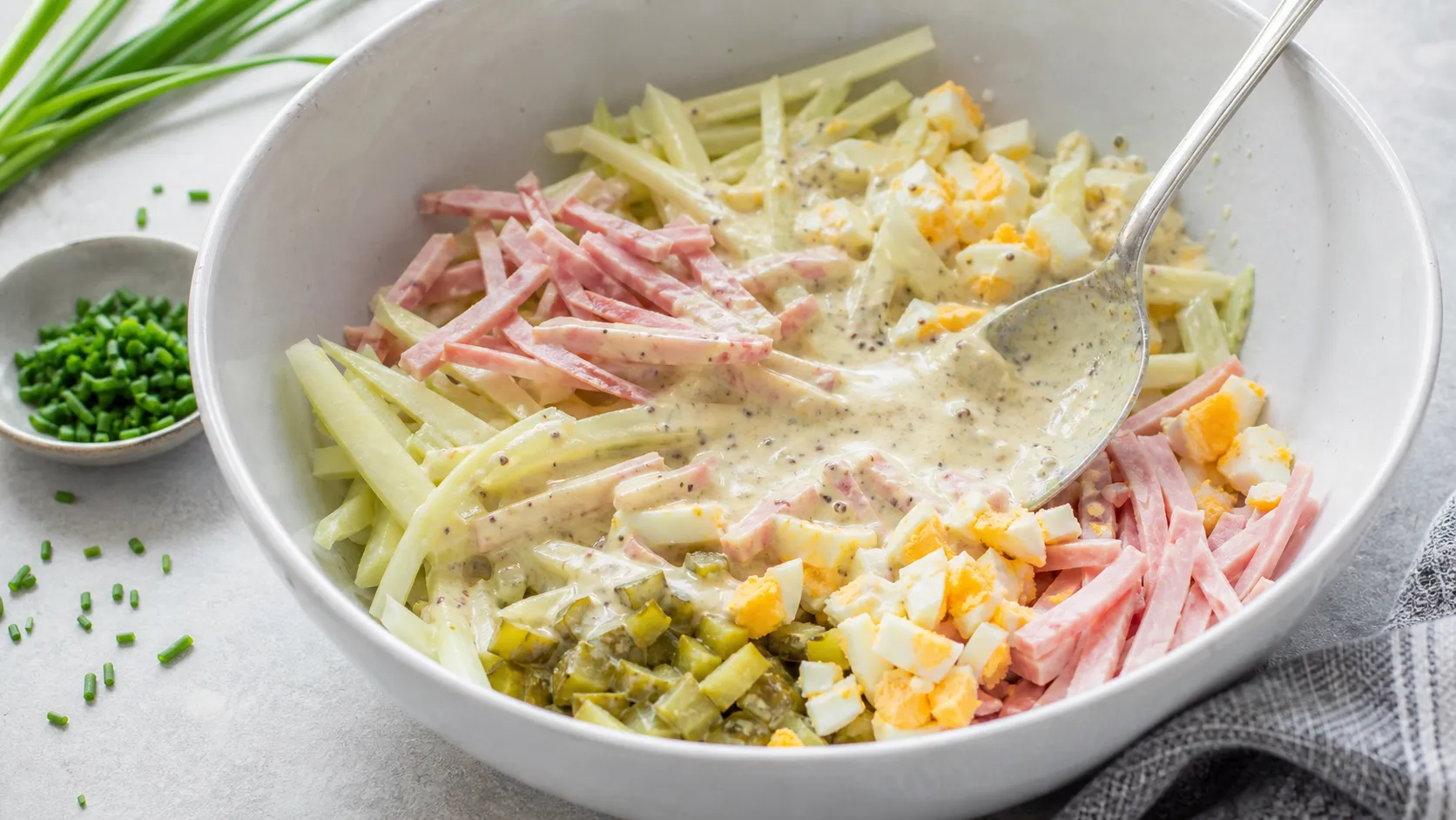 Kohlrabi cut into matchsticks being tossed with the creamy mustard dressing