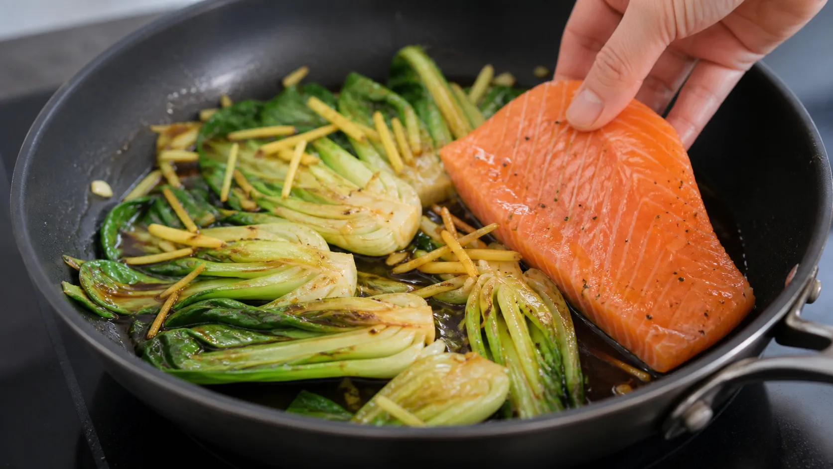 Bok choy and ginger frying in sesame oil while the salmon fillet cooks in the skillet