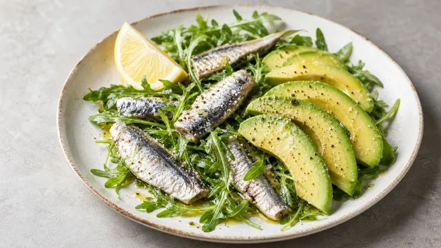 Keto sardines avocado salad with sardines in olive oil, avocado, arugula and lemon on a plate