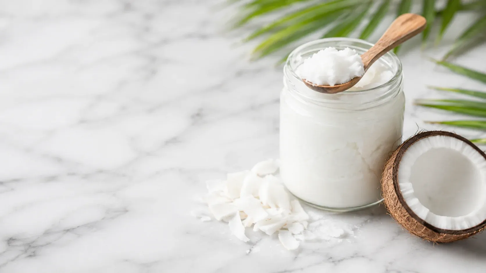 Keto food: a glass jar of white virgin coconut oil with a wooden spoon next to a halved fresh coconut